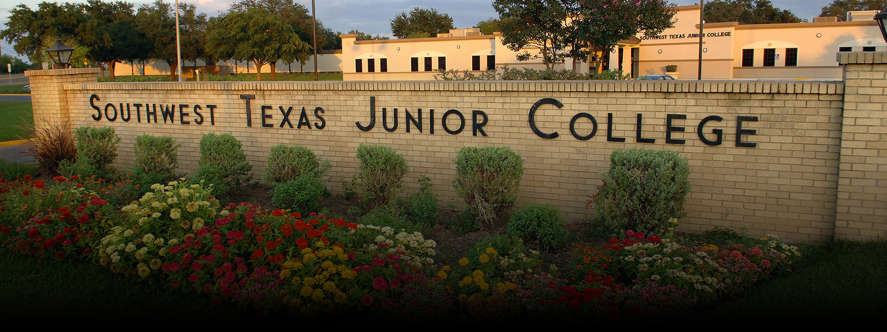 Uvalde's Southwest Texas Junior College brick wall entrance with colorful flowers planted in front of it.
